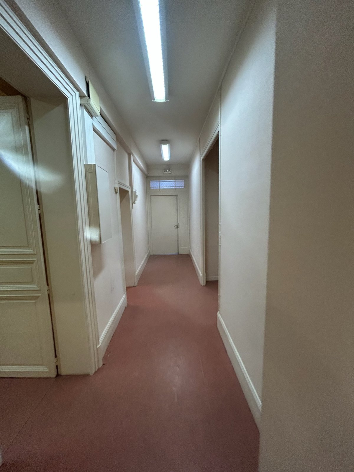 Le couloir avant travaux : sol souple rouge, tubes fluorescents apparents.