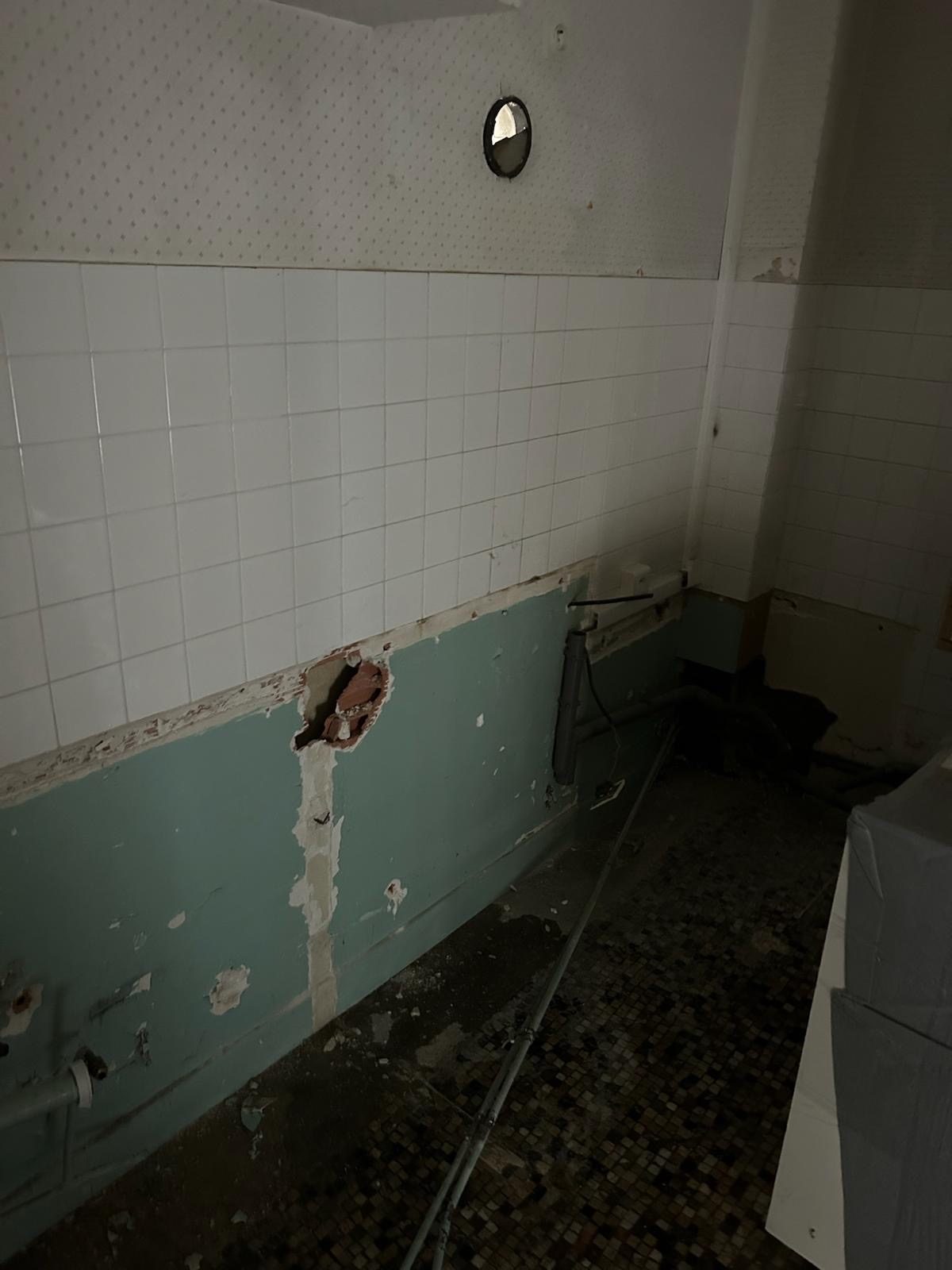 La salle de bains d’origine avant travaux : faïence blanche, soubassement vert d’eau et sol en mosaïque
